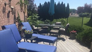 Une terrasse avec des chaises longues bleues et une table, entourée de verdure et d’un mur de briques.
