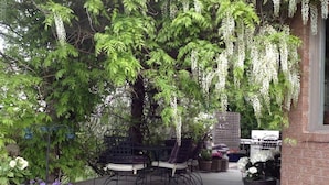 Eine Terrasse im Freien mit Tisch und Stühlen, umgeben von Topfpflanzen und weißen, hängenden Blüten.