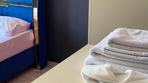 A room with a bed, a stack of towels, and a light-colored cabinet. - KARMİLİFE KONAKLAMA (Karaman)