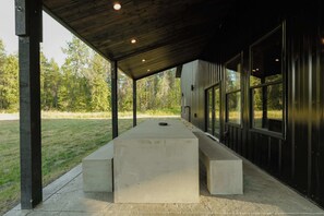 Un espace extérieur abrité, doté d’un banc en béton, de poutres en bois et de grandes fenêtres.