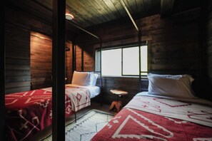 Ein Zimmer mit zwei Betten, Holzwänden, einem Fenster und einem kleinen Tisch.