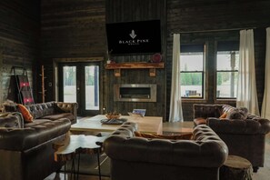A cozy living room with leather sofas, a coffee table, a fireplace, and a television mounted on the wall. - Luxe Nordic Barndominium Retreat at Black Pine (Chattaroy)