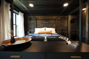 Une chambre avec un lit, une tête de lit en bois, un panneau accroché au mur et une fenêtre avec des rideaux.