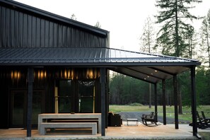 Un bâtiment moderne doté d’un patio couvert, d’un espace extérieur aménagé pour s’asseoir et offrant une vue sur un paysage boisé.