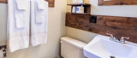 A bathroom with a toilet, sink, and wooden shelf with toiletries.