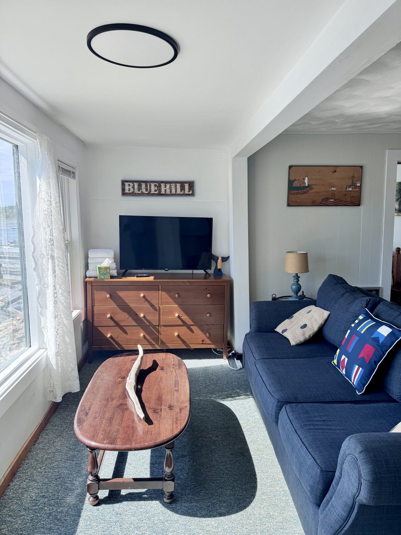 A living room with a TV, wooden dresser, blue sofa, and a wooden coffee table.