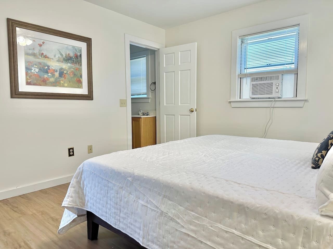Un dormitorio con una cama grande, una puerta, una ventana con persianas y aire acondicionado instalado en la pared.