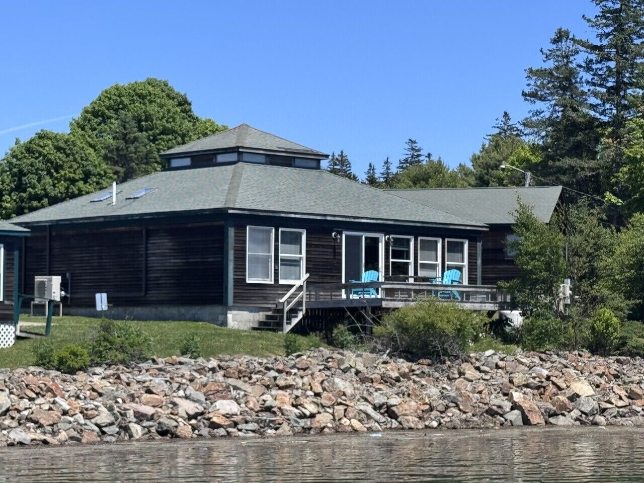 A wooden cabin with a covered deck, a small staircase, and a view of the water.