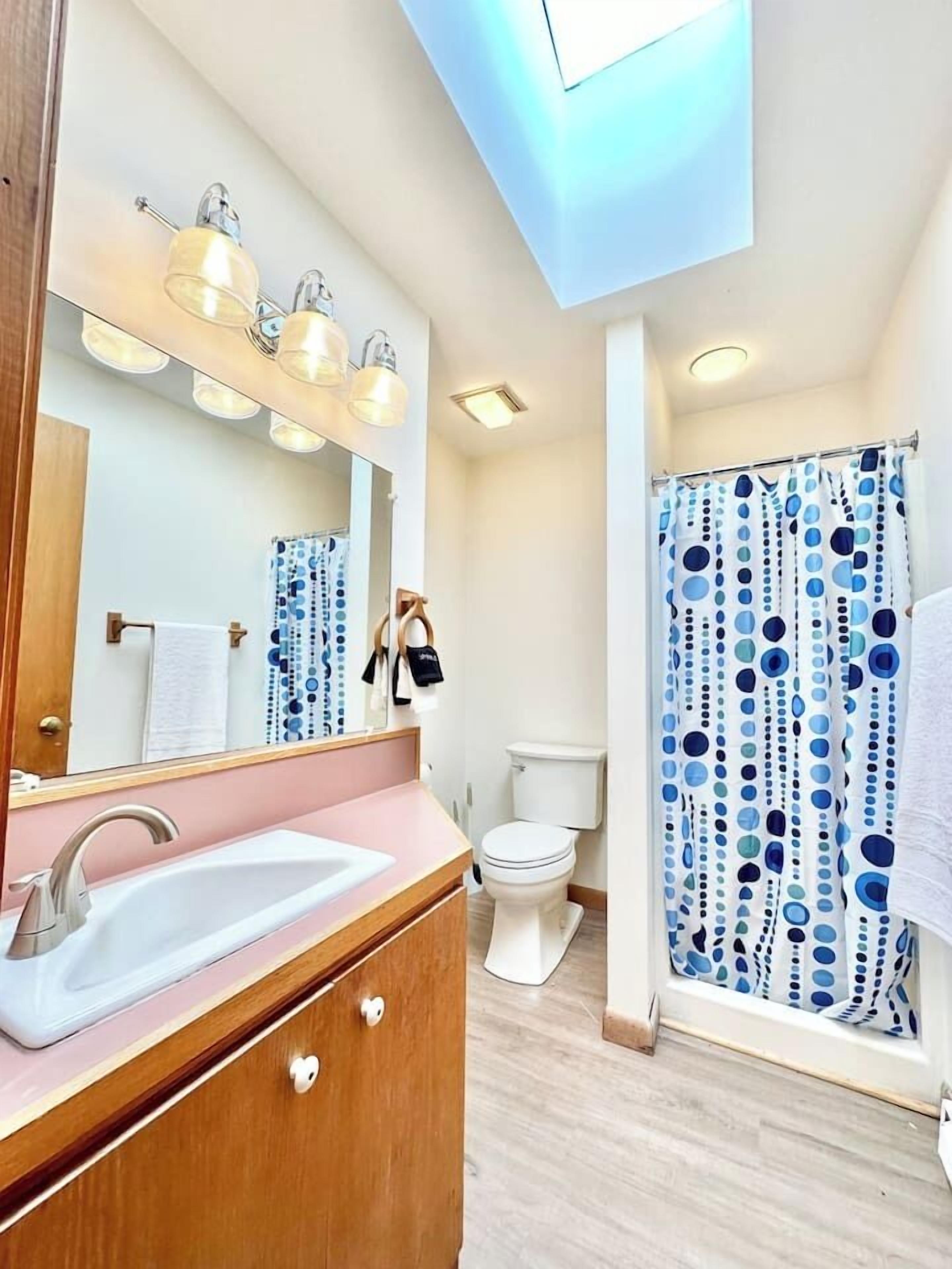 Ein modernes Badezimmer mit Oberlicht, einem Waschbecken mit Waschtisch, Toilette und einer Dusche mit Punkten.