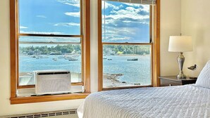 Ein Schlafzimmer mit Bett, Nachttisch, Lampe und Blick auf einen See mit Booten.