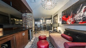 A modern kitchen with a large island, a dining area with a sofa and ottomans, and a large abstract painting on the wall.