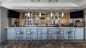A bar area with a long counter, multiple bar stools, and a bartender. Shelves with various bottles and a television are also visible. - 1-Bedroom Villa Near Disney w/ Pool & Lazy River (Kissimmee)