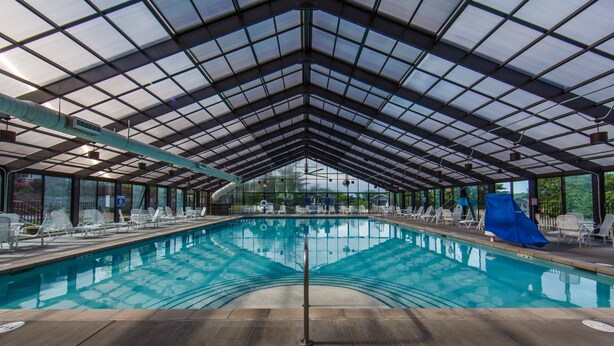 Une grande piscine intérieure dotée d’un toit en verre, entourée de chaises longues et agrémentée d’un toboggan.
