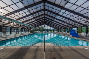 Une grande piscine intérieure dotée d’un toit en verre, entourée de chaises longues et agrémentée d’un toboggan.