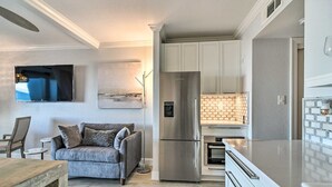 Una cocina moderna con refrigerador, horno incorporados y un comedor con mesa de madera y sofá gris.