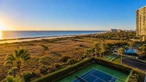 Vista costera con cancha de tenis, palmeras y un rascacielos.