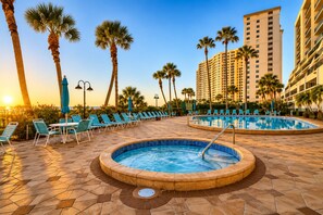 A resort pool area with lounge chairs and palm trees, surrounded by high-rise buildings. - Beachfront Sand Key Condo w/ Gulf Views (Clearwater)