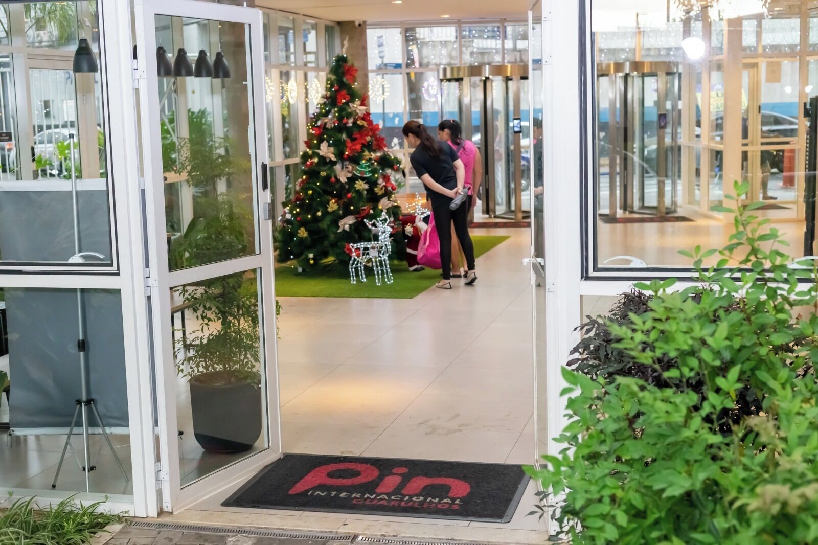 A hotel entrance with a glass door, a Christmas tree, and a doormat with the hotel's name.