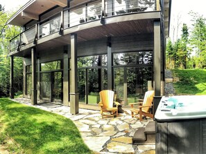 A modern house with a stone patio, outdoor seating, and a hot tub. - Le Charlevoix - Résidences boutique (Petite-Rivière-Saint-François)