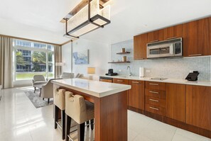 A modern kitchen with wooden cabinets, a central island, and a large window providing a view of the outdoors. - Beautiful 1/bed apartment (Miami Beach)