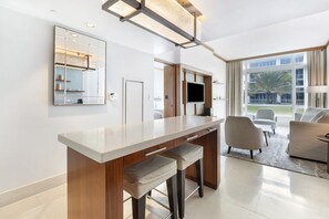 Quarto de hotel moderno com área de bar, assentos, uma janela ampla e TV de tela plana.