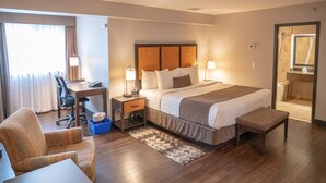 Ein Hotelzimmer mit Bett, Schreibtisch, Stuhl und einem durch eine geöffnete Tür einsehbaren Badezimmer.