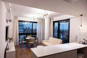 Een moderne woonkamer met een bank, eettafel en stoelen, grote ramen met gordijnen en uitzicht op de stad.