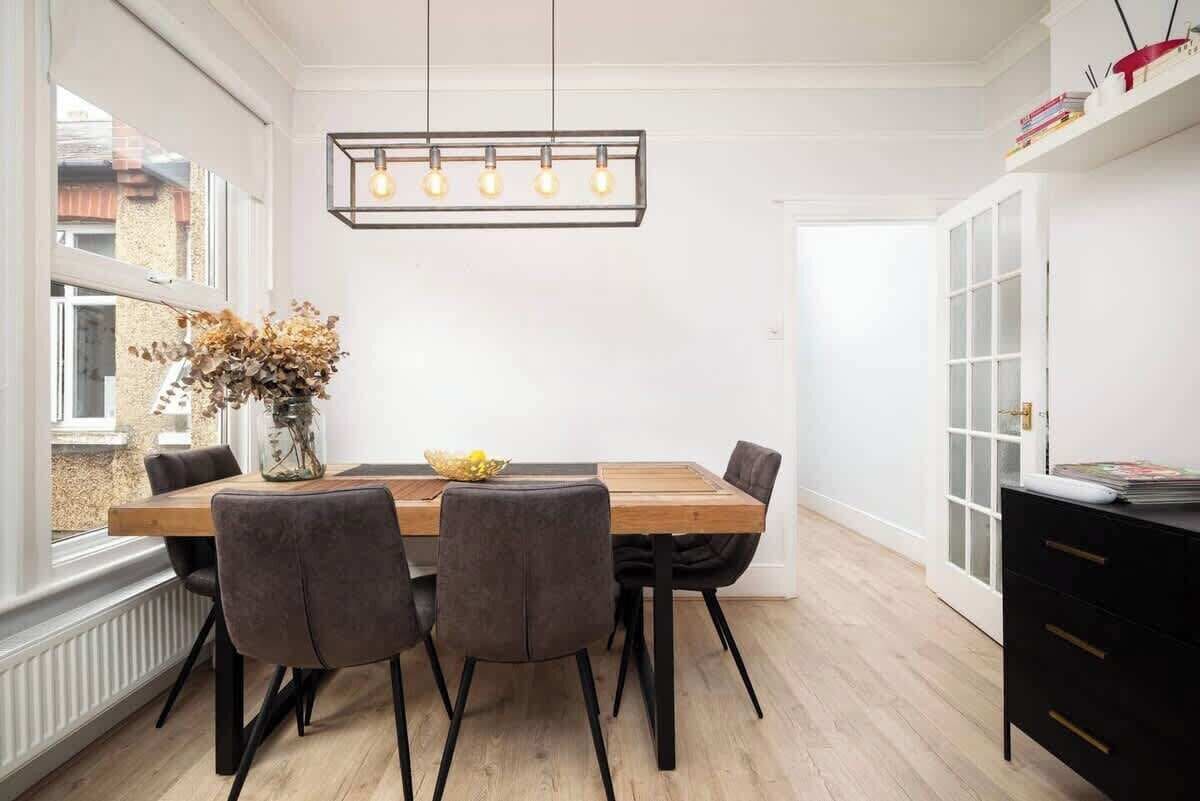 Un coin repas comprenant une table en bois, six chaises, un vase avec des fleurs séchées et un luminaire suspendu.