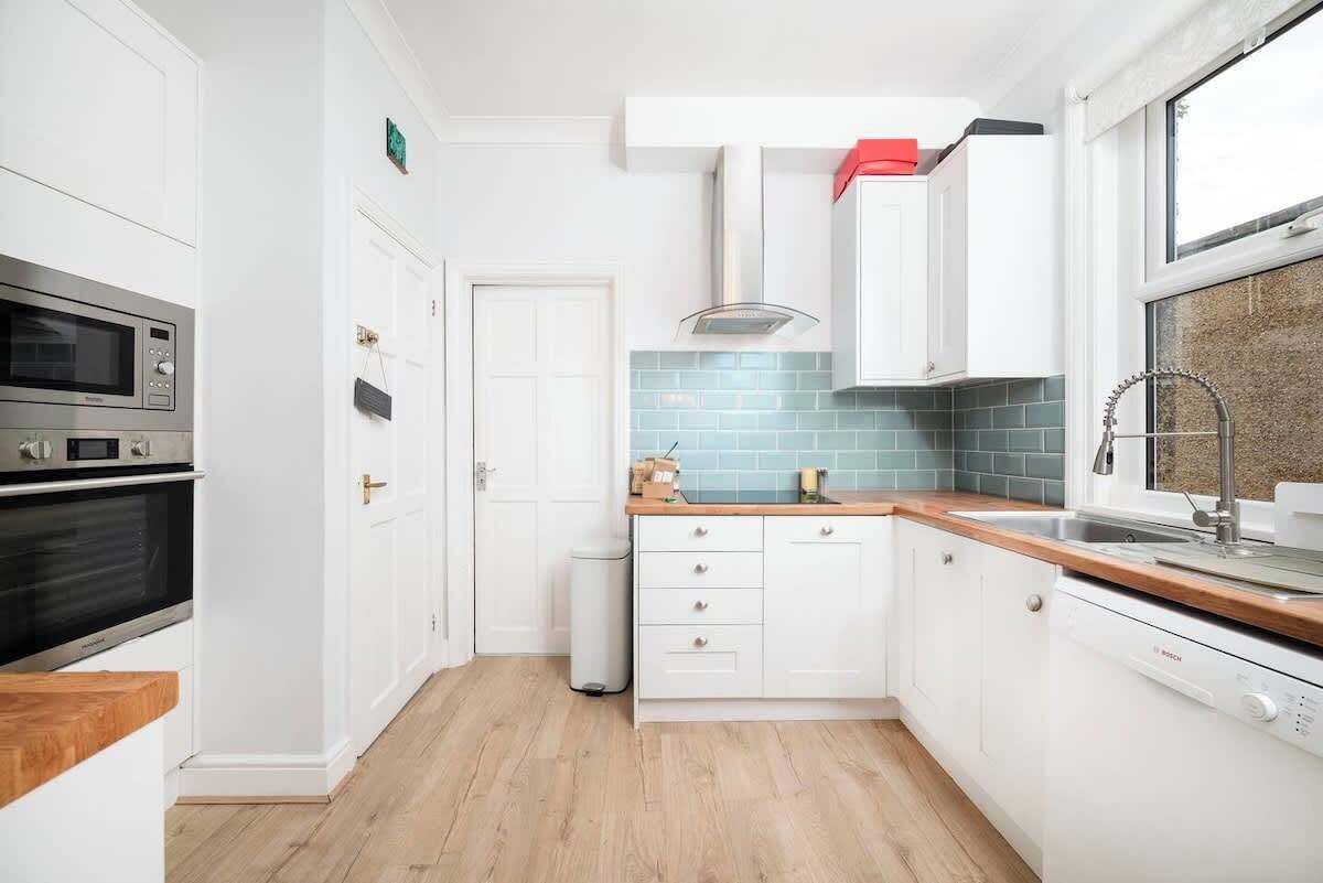 Cozinha moderna com armários brancos, máquina de lavar louça Bosch, micro-ondas e forno de aço inoxidável.