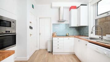Cozinha moderna com armários brancos, máquina de lavar louça Bosch, micro-ondas e forno de aço inoxidável.