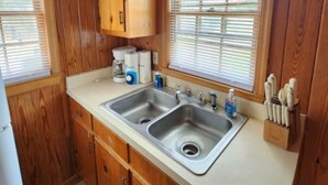 Une cuisine avec des meubles en bois, un évier à deux bacs et une fenêtre avec des stores.