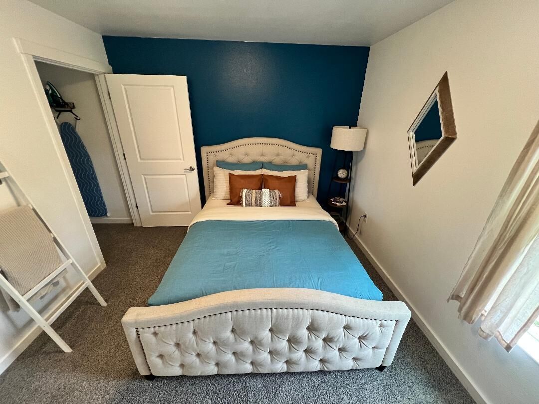 Quarto com cabeceira estofada, cama com colcha azul, porta branca e mesa de cabeceira com abajur.