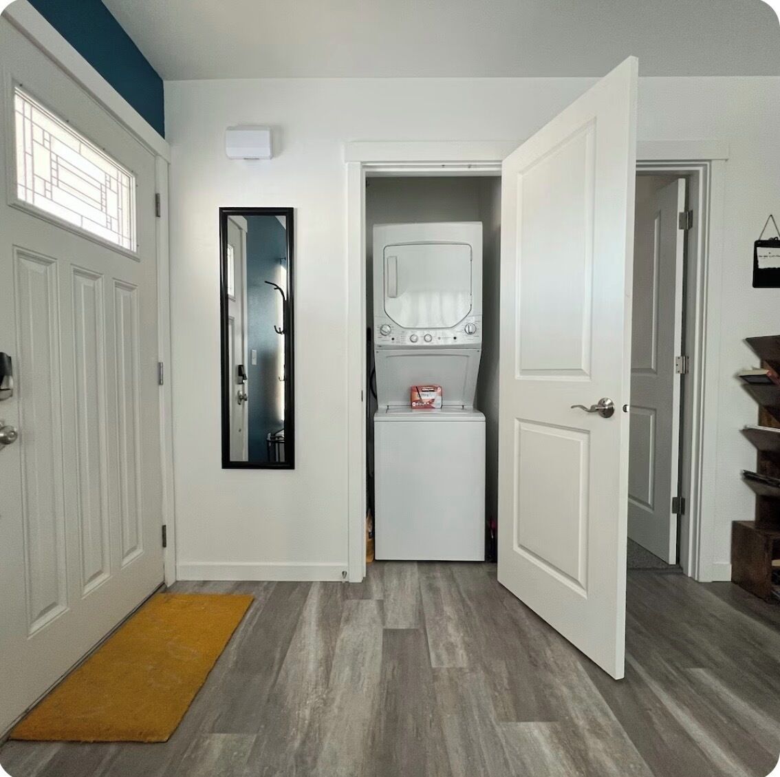 A laundry room with a washer and dryer, a mirror, and a yellow doormat.