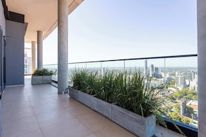 Ein Balkon mit Blick auf die Stadt, Betonpfeilern und Pflanzen in Töpfen.