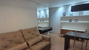 A modern living room with a brown sofa, a wooden dining table, and a TV mounted on the wall. - Conforto e Espaço privativa (Belo Horizonte)