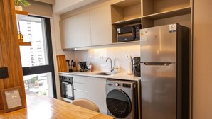 Cocina compacta con lavadora integrada, refrigerador y ventana que proporciona luz natural.