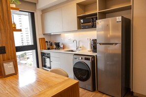 A compact kitchen with a built-in washing machine, a refrigerator, and a window providing natural light. - A luxury space designed to make you feel at home (Manora)