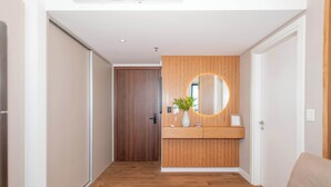 Un pasillo con suelo de madera, una pared de madera con un espejo circular, una planta pequeña y un sofá beige.
