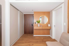 A hallway with wooden flooring, a wooden wall with a circular mirror, a small plant, and a beige sofa. - A luxury space designed to make you feel at home (Manora)