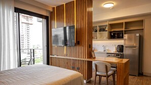 Habitación de hotel con cama, escritorio, silla, televisor y kitchenette.