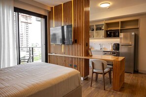 A hotel room with a bed, a desk, a chair, a television, and a kitchenette. - A luxury space designed to make you feel at home (Manora)