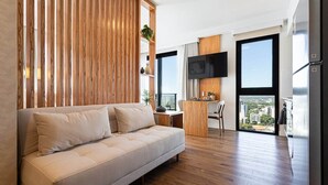 Un salón moderno con sofá, un separador de madera, televisor de pantalla plana y vistas a la ciudad a través de grandes ventanales.