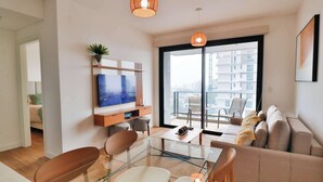 A modern living room with a glass coffee table, a sofa, a TV, and a balcony with a view of the city. - A luxury space 1BR Apartment Suite designed to make you feel at home (Asunción)