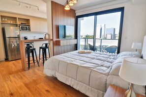 Une chambre d’hôtel moderne dotée d’un grand lit, d’une kitchenette, d’une télévision et d’un balcon offrant une vue sur la ville.