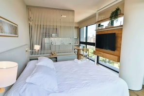 Ein modernes Hotelzimmer mit einem großen Bett, einem an der Wand befestigten Fernseher, einem Fenster mit Blick und einem dekorativen Raumteiler.
