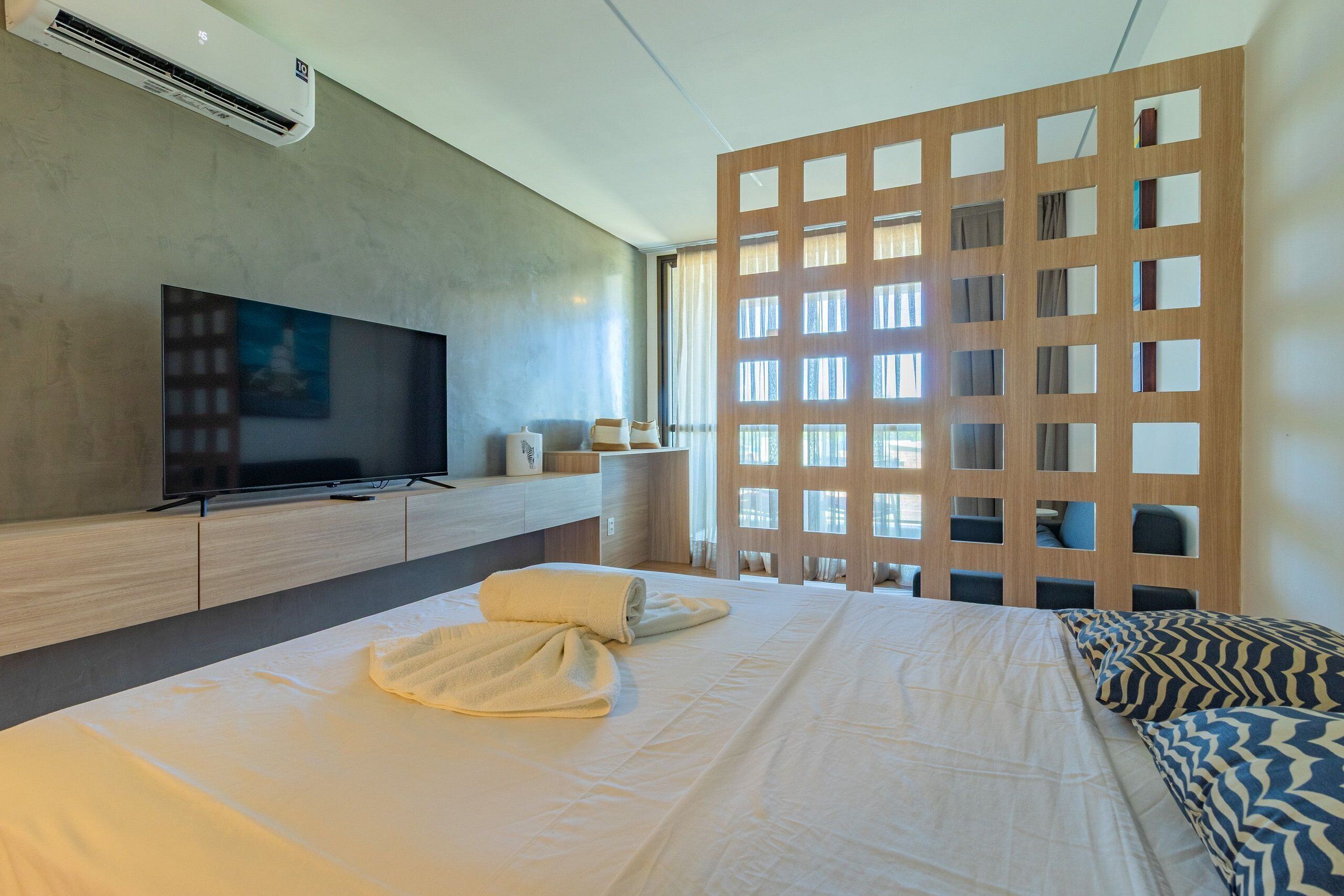 Habitación de hotel con cama, televisor, separador de madera y ventana.