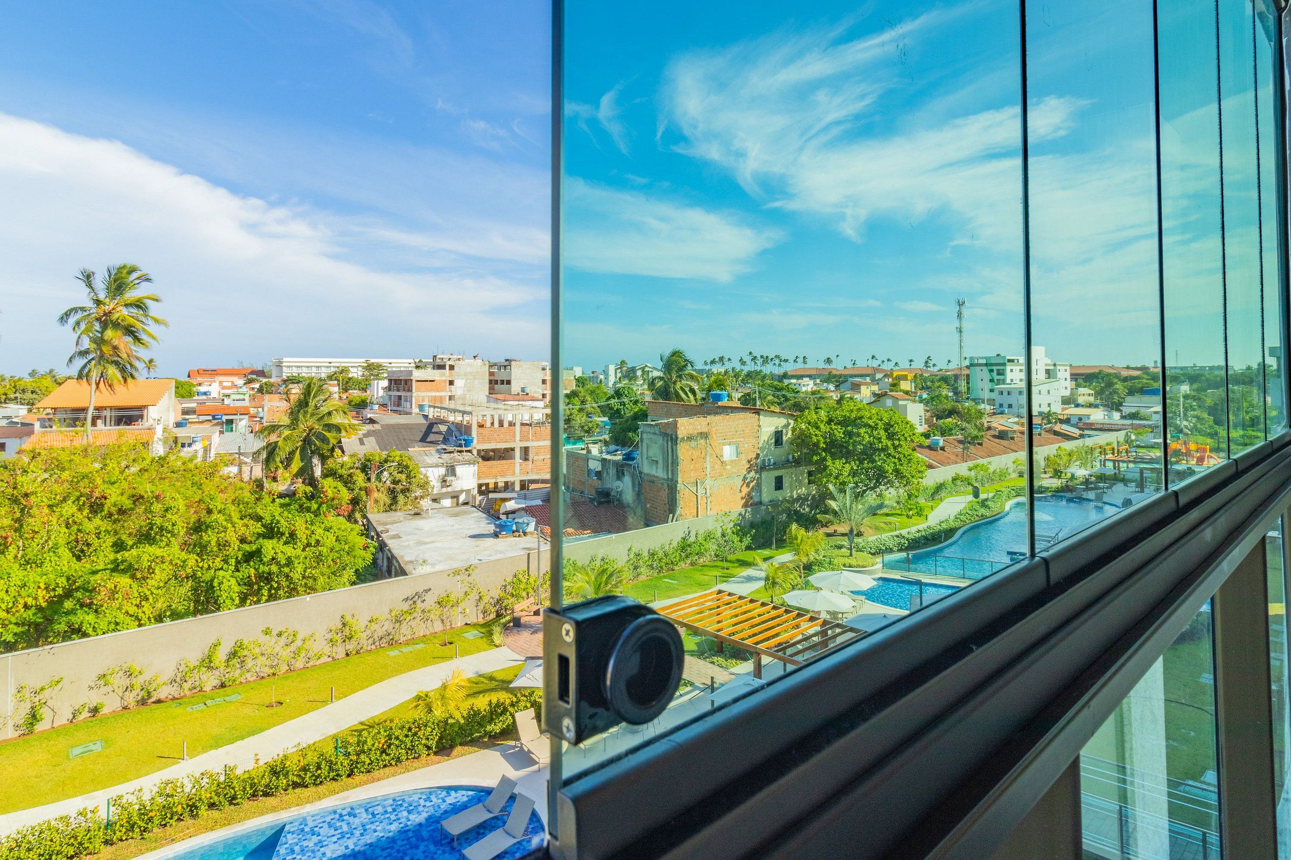 Vista da janela sobre uma piscina, vegetação e edifícios.