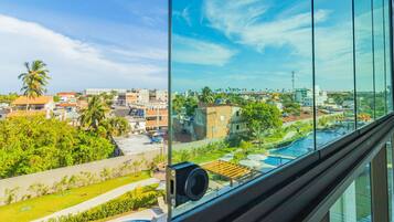 Vista da janela sobre uma piscina, vegetação e edifícios.