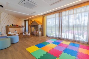 A modern room with a wooden floor, colorful foam puzzle mats, a white ceiling, and a large window with sheer curtains. - Beach Class Summer by Carpediem (Ipojuca)