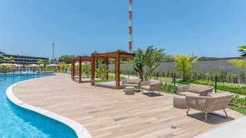 Un área junto a la piscina con terraza de madera, sillas de descanso y un pérgola.